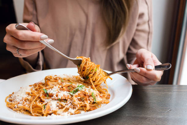 girl eats Italian pasta with tomato, meat. Close-up spaghetti Bolognese wind it around a fork with a spoon. Parmesan cheese.